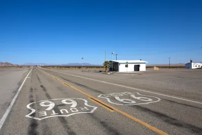 Low shot of Route 66 signs on asphalt with small abandoned building on roadside on old Route 66 near Amboy, California.