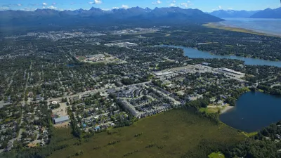 An aerial view of the Anchorage metropolitan area shows sprawling development surrounded by tall mountains.