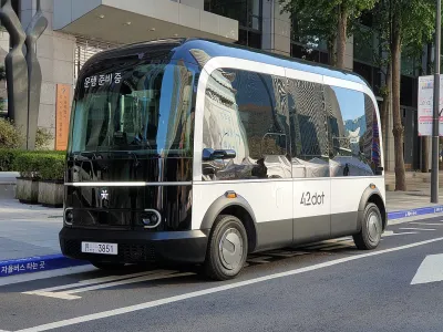 A small boxy driverless shuttle pulled up to a curb.