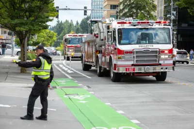 A police officer directs traffic as fire trucks arrive on scene along a street with green painted bike lanes.