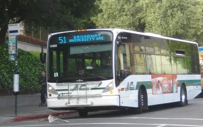 White bus pulling up to sidewalk bus station in Berkeley, California.