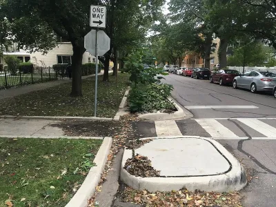 Zebra crosswalk with raised curb extensions and bioswale on small street with parked cars and mature trees.