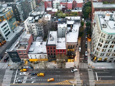 A block of the Bowery in New York City seen from high above, with taxis and other cars passing on the street in front of the buildings.
