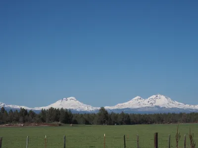 The Three Sisters, snow-covered mountains in Central Oregon, are visible in the distance beyond a farm.