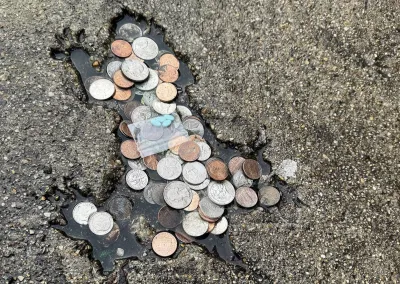 Rat shaped indentation on pavement, filled with coins