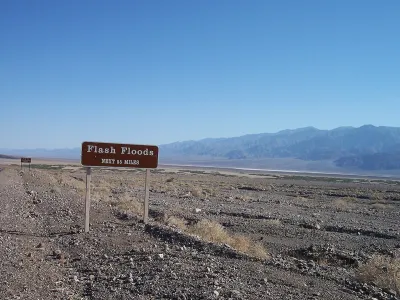 Brown and white "flash floods: next 55 miles" road sign in Death Valley, California