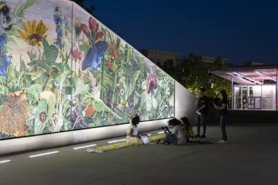 People post for photos in front of a colorful mural in the evening.