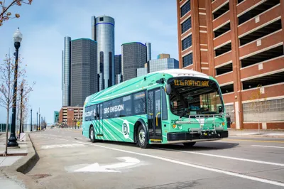 Green Detroit public transit electric bus with high-rise modenr building in background.