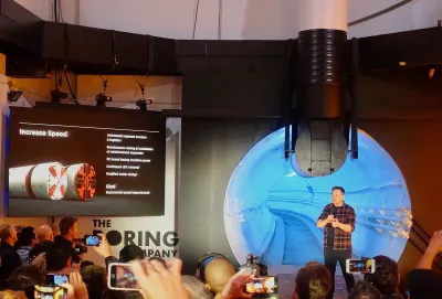 Elon Musk appears on stage in front of a backdrop of information about the Boring Company.
