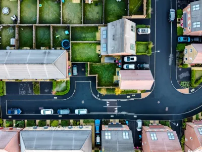 A suburban street in England, shown directly from above, with lush, green yards and driveways with cars parked in front.