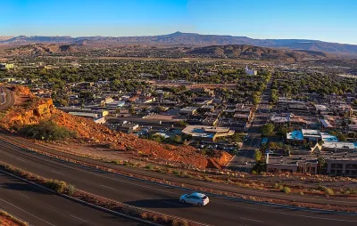 Aerial view of St. George, Utah at sunset with road in foreground and red mountains in background.