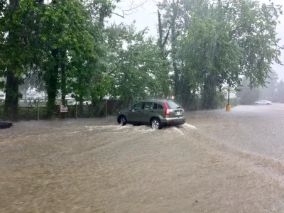 A sports utility vehicle drives throw brown floodwaters that have inundated the entire area depicted in the picture.