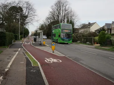 Red painted bike lane next to floating bus stop and green double-decker bus in the UK.