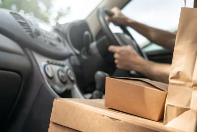 Close-up of cardboard food delivery boxes and bags on car seat next to driver.