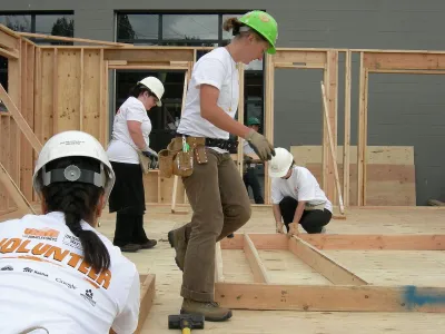 Habitat for Humanity volunteers in construction helmets buildign a wood-frame house.