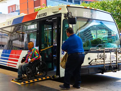 Man in wheelchair exiting public bus on ramp while operator waits outside in Houston, Texas.
