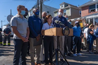 New York politicians, including Governor Kathy Hochul and Mayor Bill de Blasio, gather in front of microphones for a press conference.