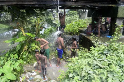 A group of young men and boys gather under water dripping from a water pipe in India.
