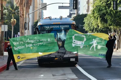 Bus driving through green banner held by two Metro employees at inauguration of new bus lane in downtown Los Angeles.