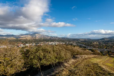 A broad valley with two tall peaks in the background. In the foregound, but far below the view from the hill where the photo was taken, large freeways are visible.