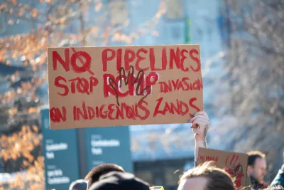 A sign held above the crowd at a protest reads "No Pipelines" and "Stop RCMP Invasion on Indigenous Lands"