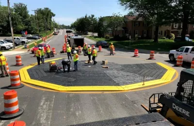 Workers in safety vests installing a black modular roundabout ringed with yellow.