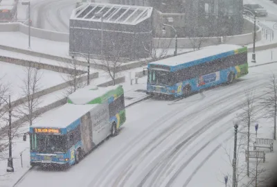 Two buses pull up to a station on a snowy day.