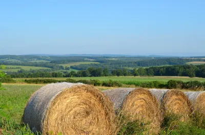 A bale if hay is rolled up in an expansive agricultural landscape.
