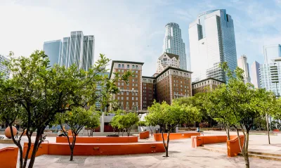 A hardscaped park with creative architectural featues is shown with the high-rises of Downtown Los Angeles in the background.