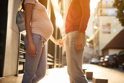 A pregnant woman holds hand with a man in an urban setting.