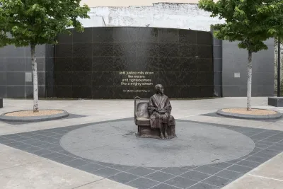 Bronze statue of Rosa Parks sitting on bus bench in center of plaza by Dallas transit station.
