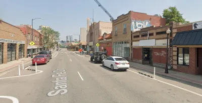 A view up Santa Fe Drive in Denver. Stores and construction are visible along the street, and Downtown Denver looms in the background.