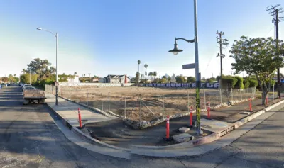 Google street view of vacant fenced-in dirt lot in South Los Angeles with graffiti on wall in background.