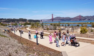 People walking on a concrete pathway at Presidio Tunnel Tops with the Golden Gate Bridge in the background