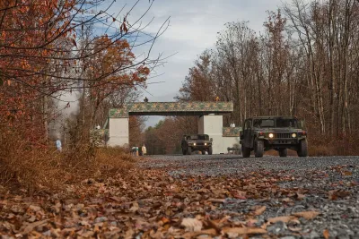 Military humvee driving through gate at Fort Indiantown Gap Natl Guard training center in Pennsylvania surrounded by winter trees and dead leaves.