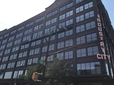 Looking up at black multi-story building with Industry City neon sign on corner.