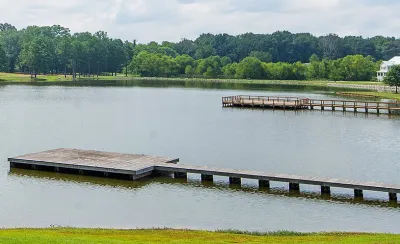 View of docks on lake surrounded by green trees and lawns with one white house at right