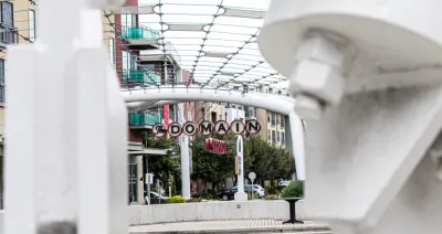 A picture of a decorative sign announcing “The Domain” surrounded by high density shops and apartments.