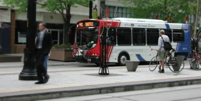 White, red, and blue Utah Transit Authority bus at stop with man standing on sidewalk next to bicycle