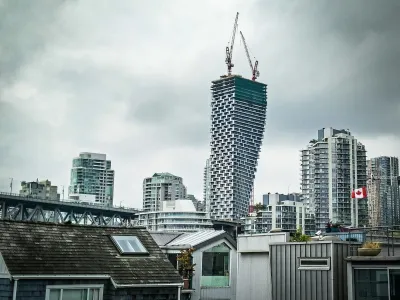 View of Vancouver House skycraper under construction with two cranes at top and other downtown Vancouver buildings surrounding it against a grey sky