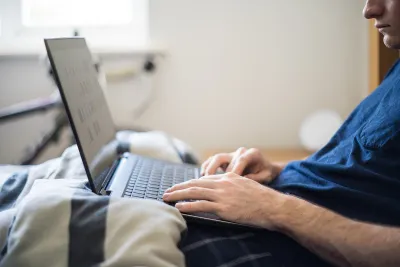A man working from home works on his laptop from bed.