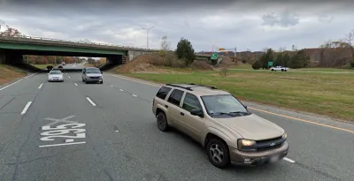 A two-lane highway cuts through a small canyon. The photo is taken from the perspective of a vehicle on the road.