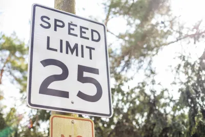 Black and white 25 mph speed limit sign on post with trees in background