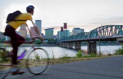 Cyclist on bike path in Portland, Oregon with bridge over river and city skyline in background.