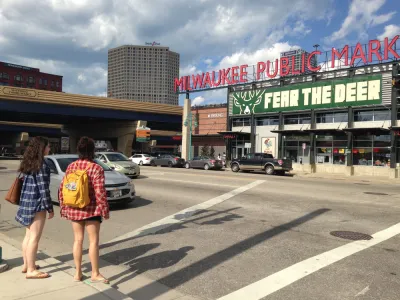 Two women waiting to cross street facing Milwaukee Public Market sign