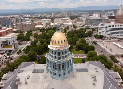Aerial view of gold Colorado state capitol building with green park and city beyond