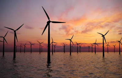 Offshore wind turbines in water against a sunset sky