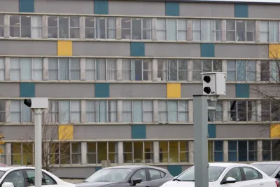 Two white traffic enforcement cameras above a road in Ottawa, Canada with a colorful multistory building in background