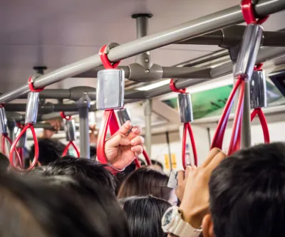 Close-up of bus passengers hanging on to red straps on crowded bus