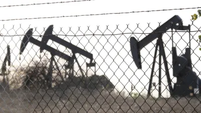 View of black oil wells behind chain link fence with barbed wire top